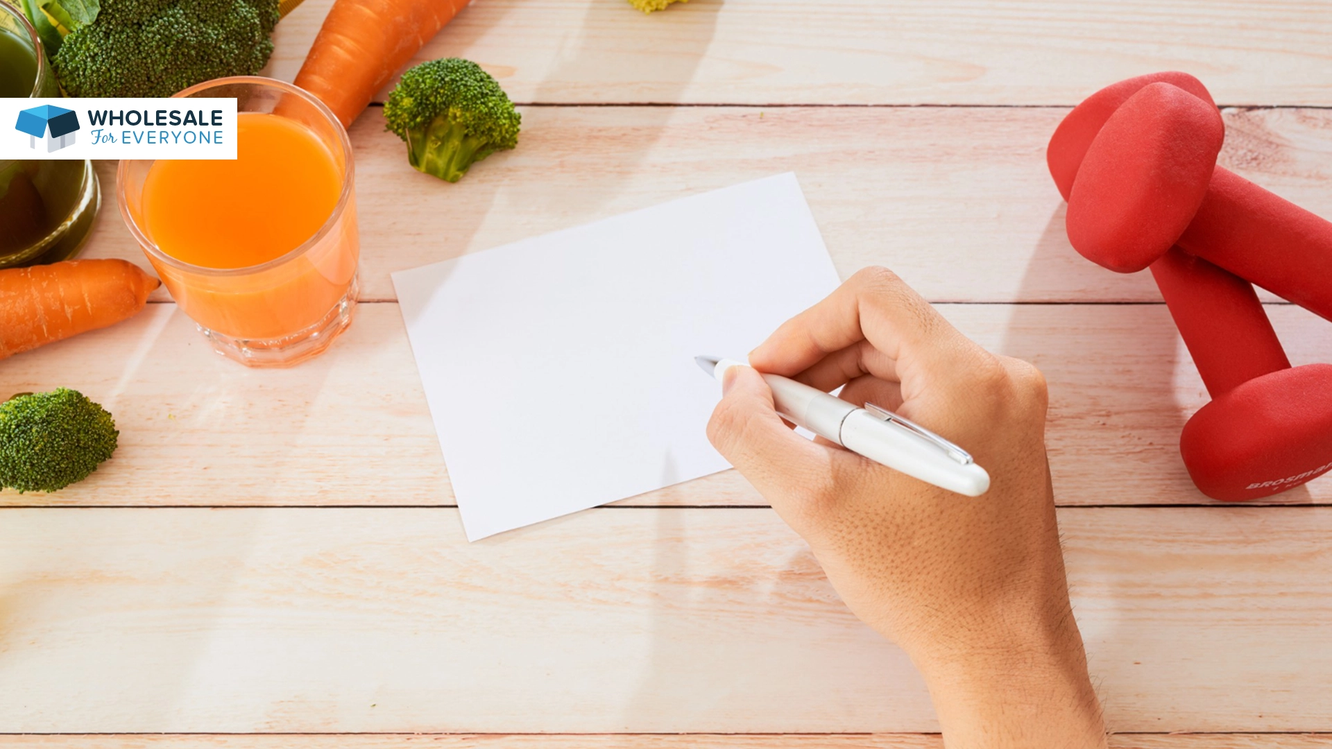 The photo shows a hand holding a pen and is about to write something on a piece of paper that is on a table with a carrot juice.