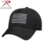 A black baseball cap features an embroidered American flag on the front. The background is plain  emphasizing the cap’s design and logo on the side.