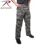 Camouflage cargo pants are being worn by a person who stands with hands on hips. The setting is plain and lacks any additional elements. The brand logo Rothco is visible in the corner.