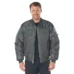 A man stands smiling while wearing a dark bomber jacket with patches and a zipper. He is in a plain white background making the focus entirely on his outfit.