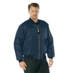A man stands confidently wearing a dark blue bomber jacket with a front zipper and pockets. The background is plain white  emphasizing the jacket's design and color.