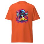 A vibrant orange t-shirt features a detailed graphic of a skull wearing sunglasses and a helmet surrounded by colorful flames and skull illustrations against a chaotic background.