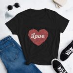 A black t-shirt features a large red heart design with the word Love prominently displayed in white. It is styled with blue jeans and black sneakers nearby.