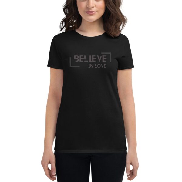 A woman wears a black t-shirt featuring the text BELIEVE IN LOVE in a bold  modern font. She stands against a neutral background  smiling with a relaxed expression.