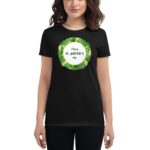 A woman wearing a black t-shirt presents a festive graphic on the front that reads Happy st. patrick's day surrounded by green shamrocks and a decorative border.