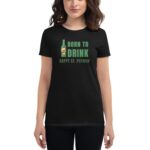 A woman wears a black t-shirt featuring the text BORN TO DRINK with a graphic of a beer bottle celebrating HAPPY ST. PATRICK against a neutral background.