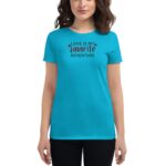 A person wears a bright turquoise t-shirt that features the text "LOVE IS MY favorite ADVENTURE" in black and red. The context is a plain background emphasizing the shirt's design.
