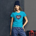 A young woman stands confidently against a dark wall wearing a bright blue t-shirt with a heart design and the word love surrounded by colorful patterns paired with loose jeans and a dark beanie.