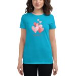 A woman wears a bright blue t-shirt featuring various pink hearts and the text Happy Valentine's Day against a neutral background  creating a cheerful and festive appearance.