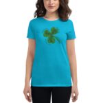 A person wears a bright turquoise t-shirt featuring a green four-leaf clover graphic with surrounding text that states various phrases about luck and love in a casual setting.