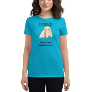 A woman wears a bright turquoise t-shirt featuring a cartoon design of a person holding a wine bottle with text saying Happy St. Patrick Wine because adulting is hard.