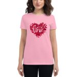 A person wears a pink t-shirt featuring a heart made of red rose petals with the word love elegantly scripted in white  standing against a neutral background.