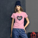 A woman stands against a textured dark wall wearing a pink t-shirt featuring a heart design with the word love surrounded by colorful floral patterns and baggy jeans with a beanie on her head.