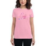 A woman wears a light pink t-shirt featuring a colorful design that spells out "Love" surrounded by decorative elements showing her smiling against a neutral background.