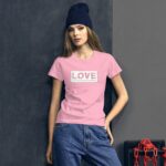 A young woman stands confidently wearing a pink t-shirt with the word LOVE printed on it and a blue beanie in front of a dark wall and a chain. Text reads: Love is the secret ingredient that makes life sweet.