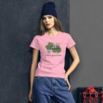 A young woman poses wearing a pink t-shirt with green text that says I LOVE MY GREENS and HAPPY ST. PATRICK. She stands against a dark background with chains nearby.