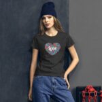 A young woman stands confidently wearing a dark t-shirt with a heart design containing colorful flowers and the word love in the center against a neutral-toned backdrop.