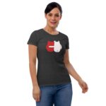 A woman wearing a dark gray t-shirt with a playful graphic of two cartoon-like characters in red and white stands with a slight smile in a neutral background.