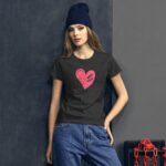 A woman poses wearing a dark t-shirt with a pink heart graphic featuring the text "SELF LOVE" on it  paired with casual denim jeans against a textured gray background.