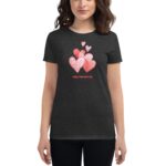 A woman wears a black t-shirt featuring a colorful heart graphic that includes pink and red hearts with various patterns and the text Happy Valentine's Day below the design.