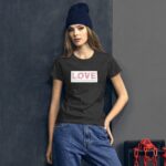 A young woman stands confidently wearing a dark t-shirt with the word LOVE printed on it and a short description below in a casual setting against a neutral background.