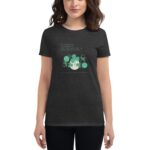 A woman stands wearing a dark t-shirt featuring green graphics of shamrocks and text celebrating St. Patrick's Day  conveying good wishes and luck associated with the holiday. Text reads: "For each petal flower You shall make a wish Good health good luck and happiness Each day of your life HAPPY ST. PATRICK'S DAY"