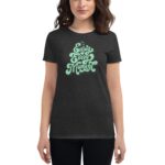 A woman wearing a dark t-shirt displays a playful green text design that reads Enjoy Every Moment in a casual indoor setting.