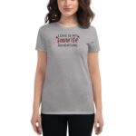 A woman wearing a gray t-shirt displays the text "LOVE IS MY favorite ADVENTURE" in playful fonts and red hearts  standing against a neutral background.