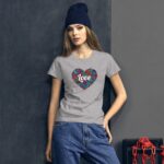 A young woman poses against a dark background wearing a gray t-shirt featuring a colorful heart design with the word love and blue beanie while dressed in casual jeans.