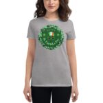 A woman wears a gray t-shirt featuring a circular design with shamrocks and the phrase "HAPPY St. Patrick's Day" alongside a green hat and glasses  celebrating the holiday.