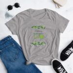 A gray t-shirt with the text Happy St Patrick's Day decorated with green shamrocks lies on a flat surface next to blue jeans and black sneakers  evoking a festive mood.