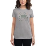 A grey t-shirt features a festive design with green and gold clovers and hats surrounding the text "Happy St. Patrick's Day" at its center  worn by a woman standing casually.