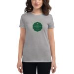 A woman wears a gray t-shirt featuring a green oval graphic with the text Life's like a cup of tea surrounded by floral designs  standing in an undefined indoor setting.