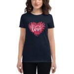A dark navy t-shirt features a heart shape made of red rose petals with the word love scripted in white at the center the wearer stands casually with a neutral expression.