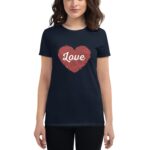 A woman stands wearing a navy blue t-shirt featuring a red heart graphic with the word Love in white across the center against a neutral background.