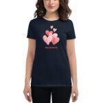 A woman is wearing a dark navy t-shirt featuring colorful heart graphics above the text Happy Valentine’s Day in red. The setting is casual and festive.