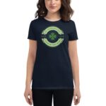 A dark t-shirt features a green circular design with a shamrock in the center displaying the text St. Patrick's Day Love Luck Luck of the Irish around it worn by a woman standing in a neutral setting.