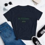 A dark navy t-shirt with the text "HAPPY St. Patrick's DAY" is positioned on a light surface next to denim jeans and black sneakers  creating a casual outfit for the holiday.