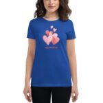 A blue t-shirt features a graphic of several colorful hearts and the text Happy Valentine's Day while being worn by a person with loose  wavy hair.