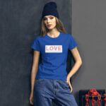 A young woman stands confidently wearing a blue shirt with the word LOVE prominently displayed on the front in a casual setting next to a dark wall and red chains. Text: Love is the secret ingredient that makes life sweet.