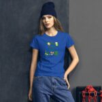 A woman wearing a blue t-shirt with a festive St. Patrick's Day design stands against a dark wall. Her expression is neutral  and she pairs the shirt with denim jeans and a beanie.