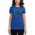 A woman wears a blue t-shirt featuring a green graphic design with the text Life's like a cup of tea surrounded by plant illustrations  standing in a neutral setting.