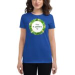 A woman wears a blue t-shirt with a circular design featuring green leaves and the text Happy st. patrick's day in the center  set against a neutral background.