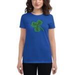A woman wearing a blue t-shirt stands confidently with a green shamrock graphic on the front surrounded by positive words symbolizing luck and love in a neutral background.