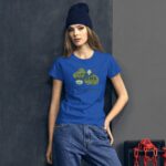 A woman wearing a blue t-shirt with a green graphic design stands against a dark wall. She has long hair and is wearing a dark beanie while posing confidently. The shirt features the text "I LOVE MY GREENS" and "HAPPY ST. PATRICK."