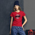 A young woman stands against a textured wall wearing a red t-shirt with the word LOVE and floral designs while sporting a dark knit beanie her relaxed pose suggests confidence in an urban setting