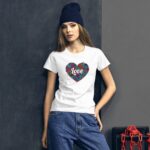 A woman leans against a textured dark wall wearing a white t-shirt featuring a heart design with the word love in the center paired with loose blue jeans and a dark beanie.