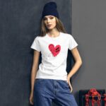 A young woman stands confidently wearing a white t-shirt with a pink heart graphic featuring text "SELF LOVE" alongside a figure. She is in casual denim jeans and a black beanie against a dark wall.