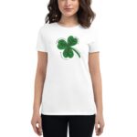 A woman is wearing a white t-shirt featuring a green four-leaf clover graphic with surrounding text expressing themes of good luck in business and love set against a neutral background.
