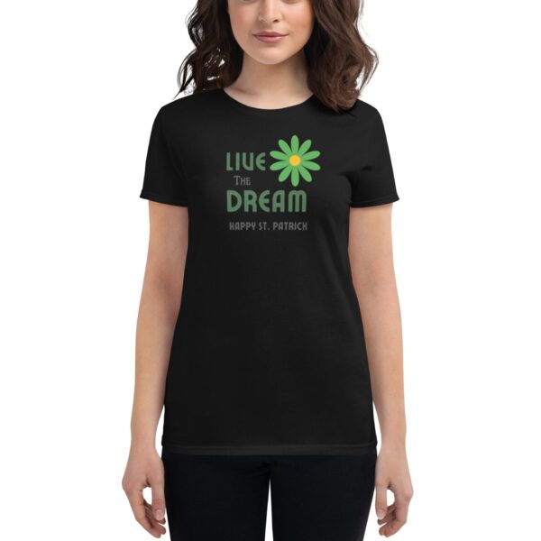 A woman wears a black t-shirt featuring the text "LIVE THE DREAM" with a green daisy and "HAPPY ST. PATRICK" below it in a casual setting.